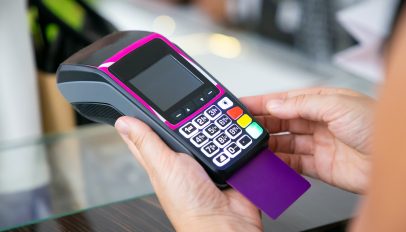 Clothes store cashier operating payment process with pos terminal and credit card. Cropped shot, closeup of hands. Shopping or purchase concept